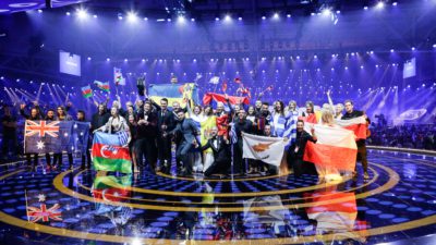 De tio vinnarna står i en klunga med sitt lands flagga i händerna. I bakgrunden är det massa strålkastare.