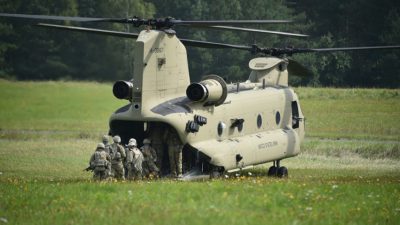 En grön stor helikopter står på en gräsmatta. Flera soldater håller på att gå in i helikoptern.