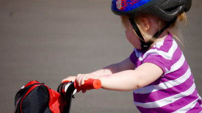 Ett litet barn, kanske 3-4 år, som sitter på en liten cykel. Barnet har hjälm och randig tröja.