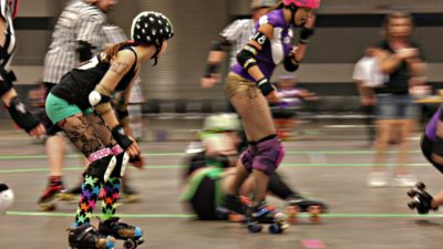 Några personer susar förbi på rullskridskor. De har korta shorts, knä- och armbågsskydd, hjälm och färgglada kläder.