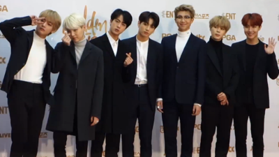 De sju bandmedlemmarna står framför en vit vägg. De har svarta kostymer på sig, några har vita tröjor under. De har alla korta frisyrer, men som är lite längre och hänger ner på pannan och på sidorna. En vinkar, en annan göra peacetecknet och några andra bara ler mot kameran.