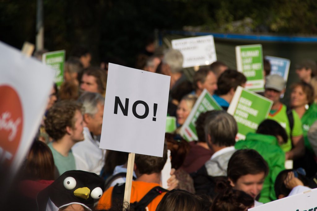 Flera politiska budskap syns på skyltar i en stor folkmassa. På skylten längst fram står det "NO!" som i "Nej!".