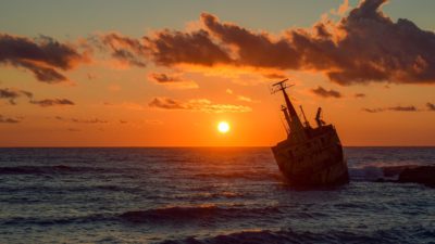 Bild på en båt som seglar i solnedgången. På havet syns vågor och det är några enstaka moln på himlen.