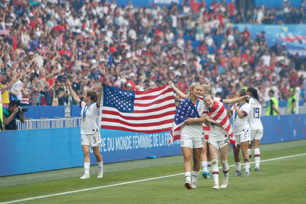 USA:s lag springer längs med kanten av planen. De håller upp en stor amerikansk flagga, vinkar åt publiken och kramar varandra.