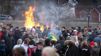 Foto på folksamling som står runt en stor brasa.