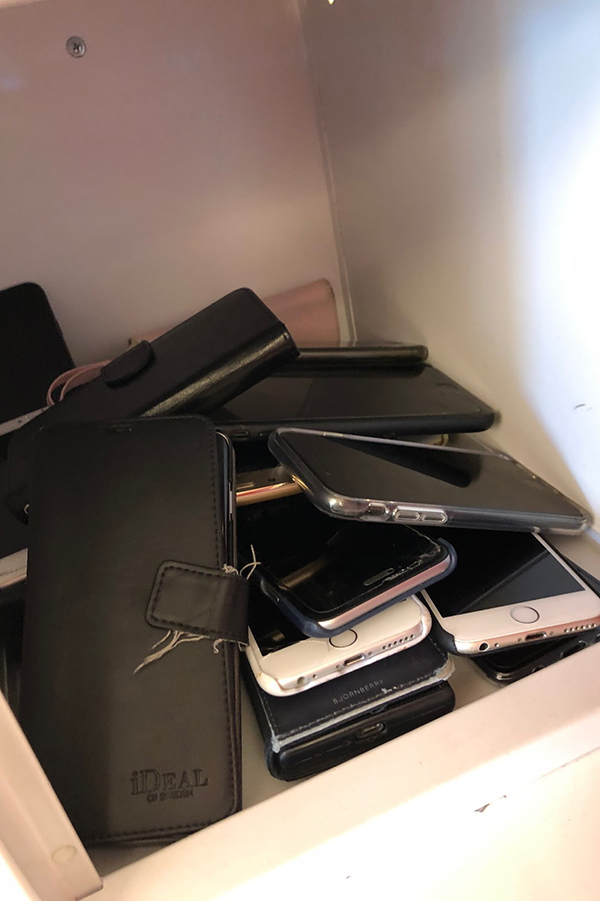 Foto på en hög med mobiltelefoner i ett skåp.