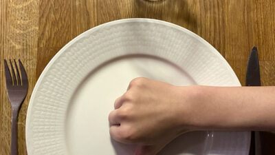 En tom tallrik med en hand på som gör tummen ner.